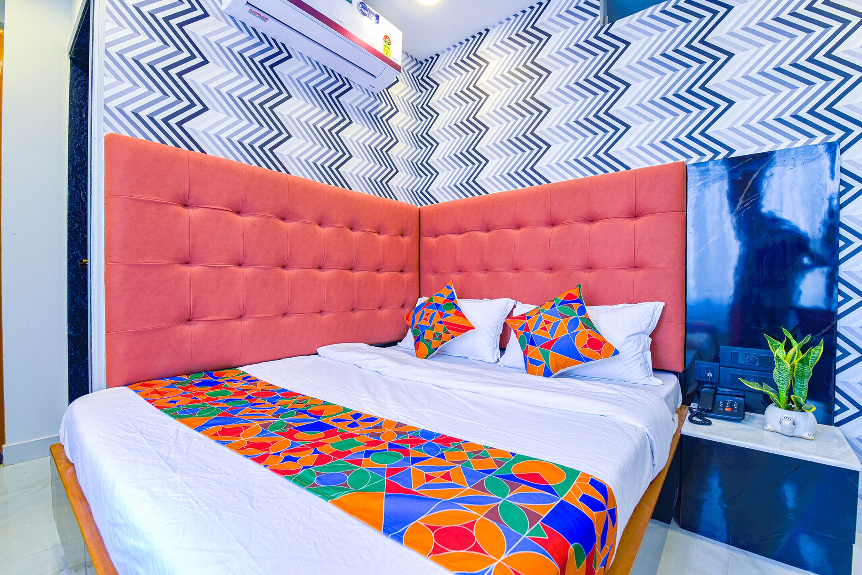 Un dormitorio moderno con una llamativa cabecera naranja, una colcha de cama con motivos geométricos y un papel tapiz estampado.