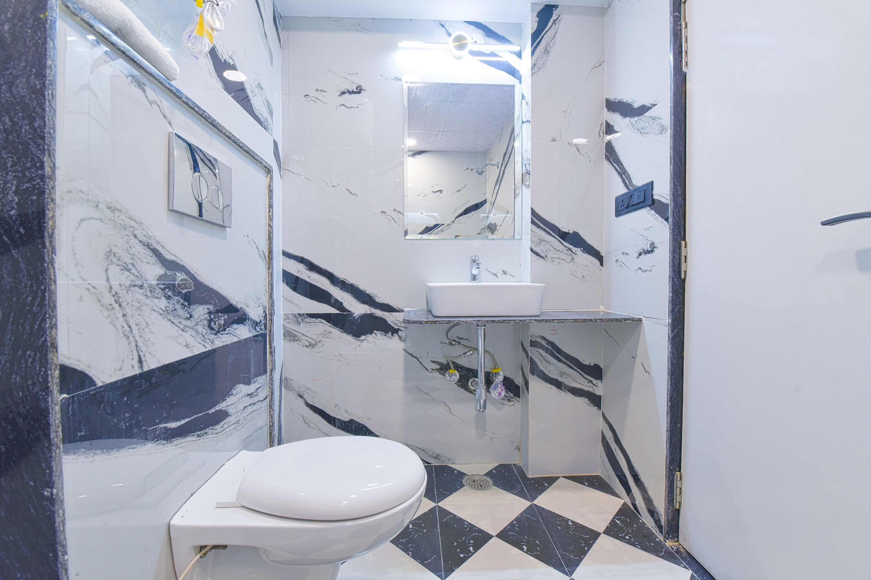 A bathroom with a white toilet, a sink, and a mirror. The walls and floor have a marble pattern.