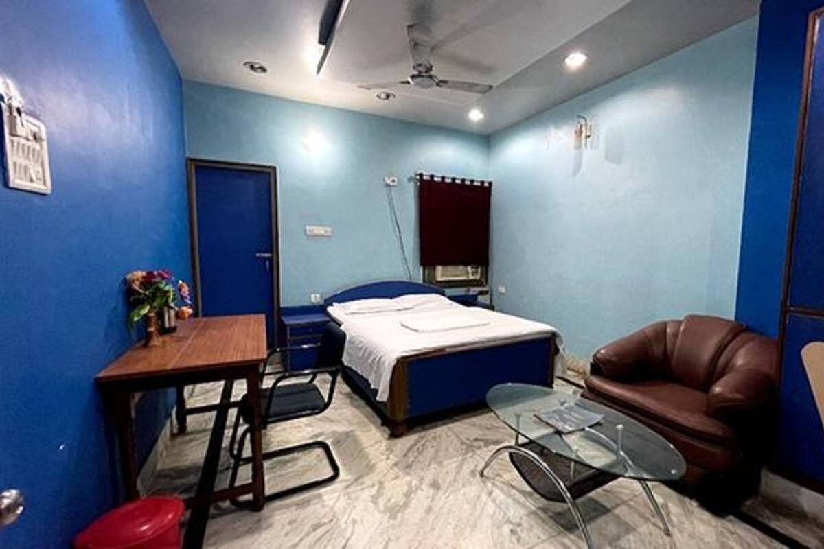 A bedroom with a bed, a desk, a chair, a glass table, and a leather couch.
