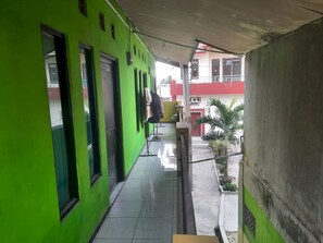 A narrow corridor with green walls, a tiled floor, and a covered area with a concrete wall. - OYO Life  93023 Kost Bulan Karawang (Karawang)