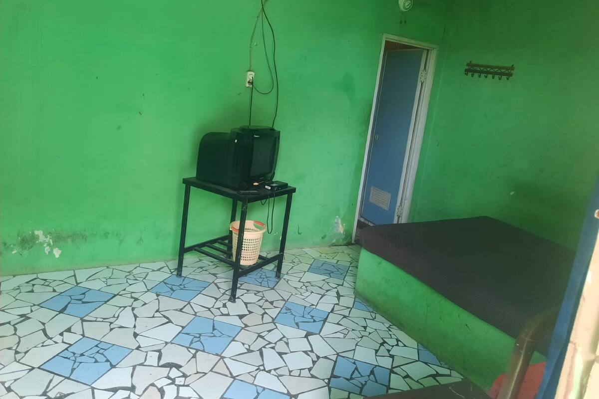 A room with a green wall, a tiled floor, a small table with a television, a door, and a bed.