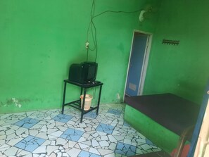 A room with a green wall, a tiled floor, a small table with a television, a door, and a bed. - OYO Life  93023 Kost Bulan Karawang (Karawang)