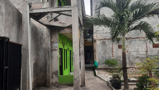 A narrow alleyway with a green door, concrete walls, and a palm tree. - OYO Life  93023 Kost Bulan Karawang (Karawang)