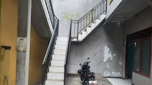 A narrow alley with a motorcycle parked at the bottom, a staircase leading upwards, and a door with a green frame on the right. - OYO Life  93023 Kost Bulan Karawang (Karawang)