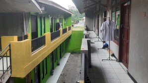 A corridor with a green and yellow building, a white table, and a white coat hanging on a stand. - OYO Life  93023 Kost Bulan Karawang (Karawang)