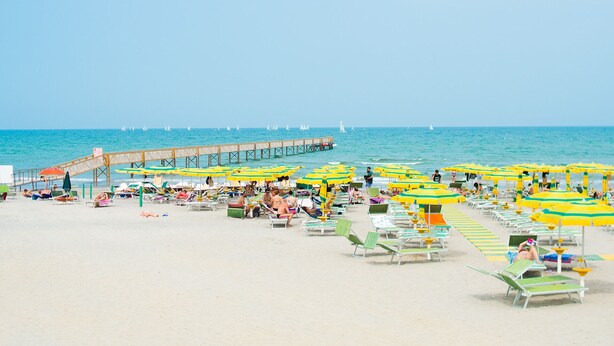 A beach with rows of sunbeds and umbrellas, a pier extending into the sea, and sailboats in the background. - Comfortable, fully equipped, 2-bedroom, 2-bathroom mobile home, Cesenatico beach (Cesenatico)
