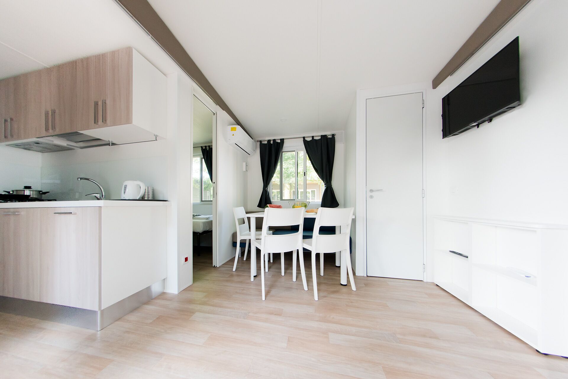 Une cuisine compacte avec un coin repas, un téléviseur fixé au mur et une vue sur l’extérieur par la fenêtre.