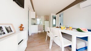 A modern kitchen with white cabinets, a dining table with chairs, and a breakfast setup with orange juice and a watermelon slice. - Comfortable, fully equipped, 2-bedroom, 2-bathroom mobile home, Cesenatico beach (Cesenatico)