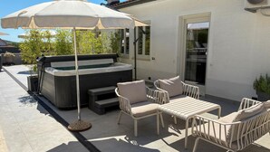 Un patio con jacuzzi, mobiliario exterior y una sombrilla grande.