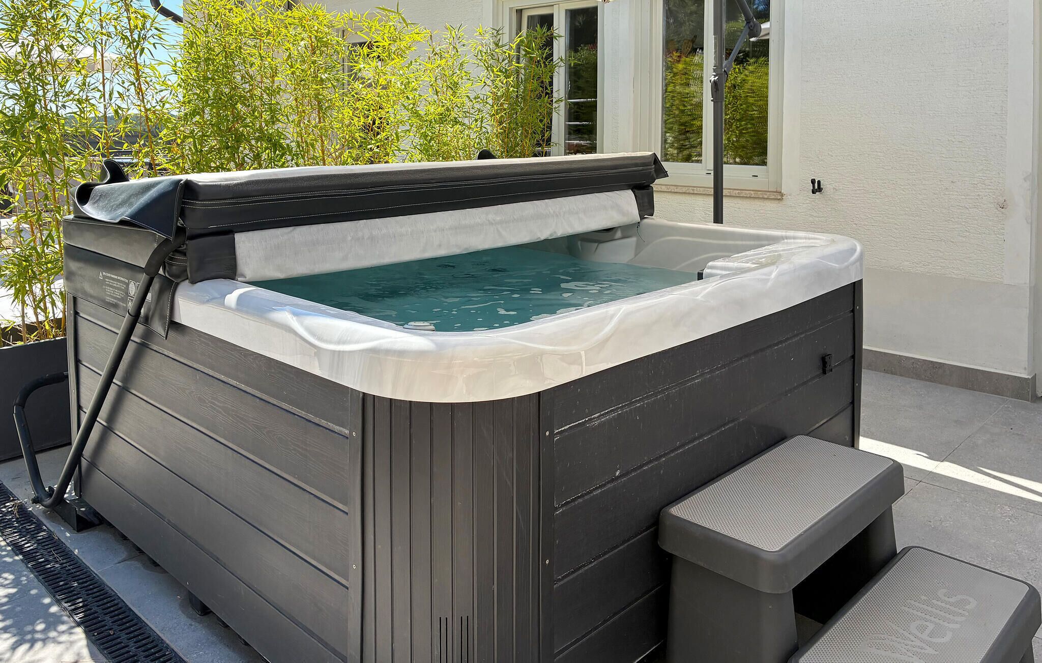 A hot tub with a bench and a step, surrounded by a house and greenery.