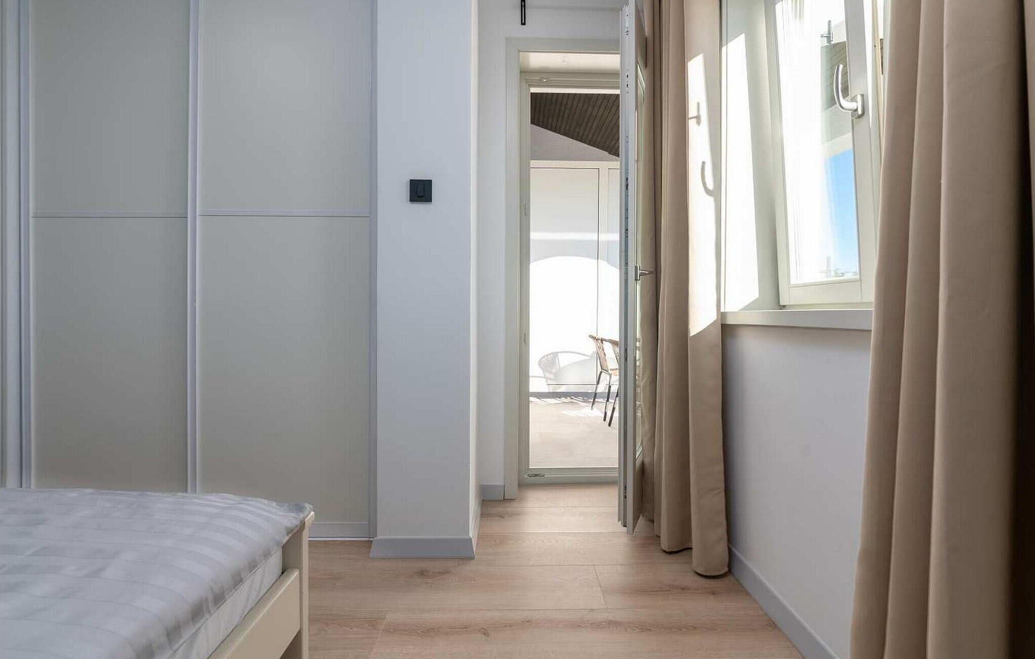 A narrow hallway with a bed on the left and a window with curtains on the right.