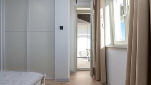 Un pasillo estrecho con una cama a la izquierda y una ventana con cortinas a la derecha.