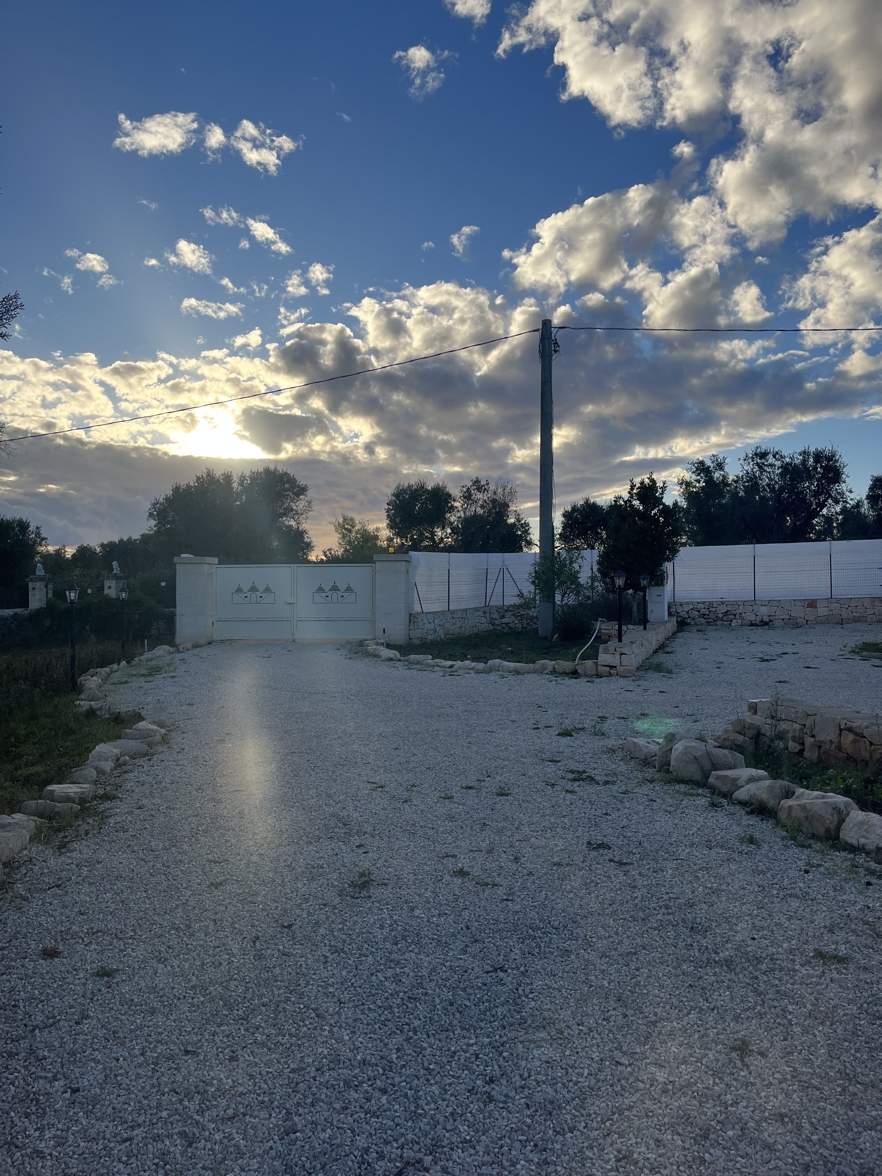 A gravel path leading to a gated area with a stone wall and a fence.