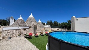 Ein Schwimmbecken mit Liegestühlen und ein Steinhaus mit Kegeldächern.