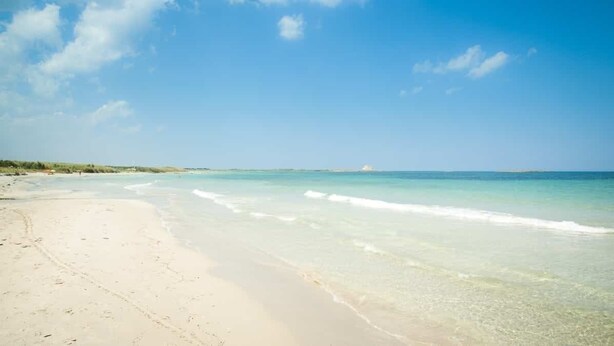 Ein Strand mit klarem türkisblauem Wasser und einem sandigen Ufer.
