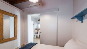 Une chambre à coucher comprenant un lit, un miroir à cadre en bois, une étagère bleue et une porte donnant sur un coin repas.