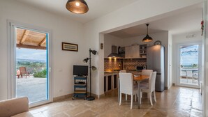 Un vaste espace de vie avec une porte-fenêtre coulissante donnant sur un balcon, un coin repas avec une table et des chaises, et une cuisine équipée d’appareils modernes et dotée d’un crédence décorative.