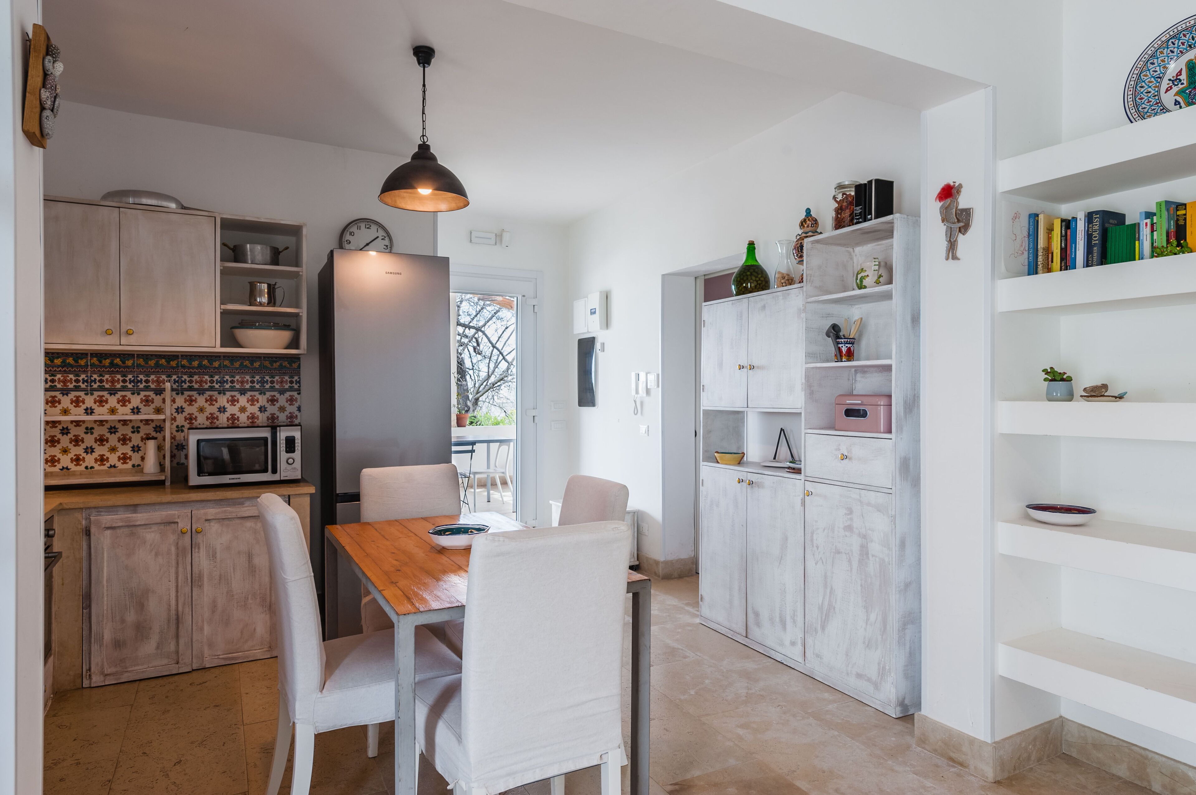 Une cuisine moderne avec des meubles blancs, une table à manger en bois et un luminaire suspendu.