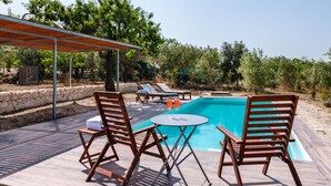 Un espace aménagé au bord de la piscine, avec un mur en pierre, des chaises longues en bois et une table sur laquelle se trouvent une bouteille et des verres.