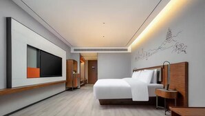 Ein modernes Hotelzimmer mit einem großen Bett, einem Flachbildfernseher, einem Holzkopfende und einem an der Wand befestigten Kunstwerk.