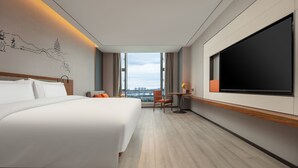 Een moderne hotelkamer met een groot bed, een bureau met stoel, een flatscreen televisie en uitzicht op de skyline door grote ramen.