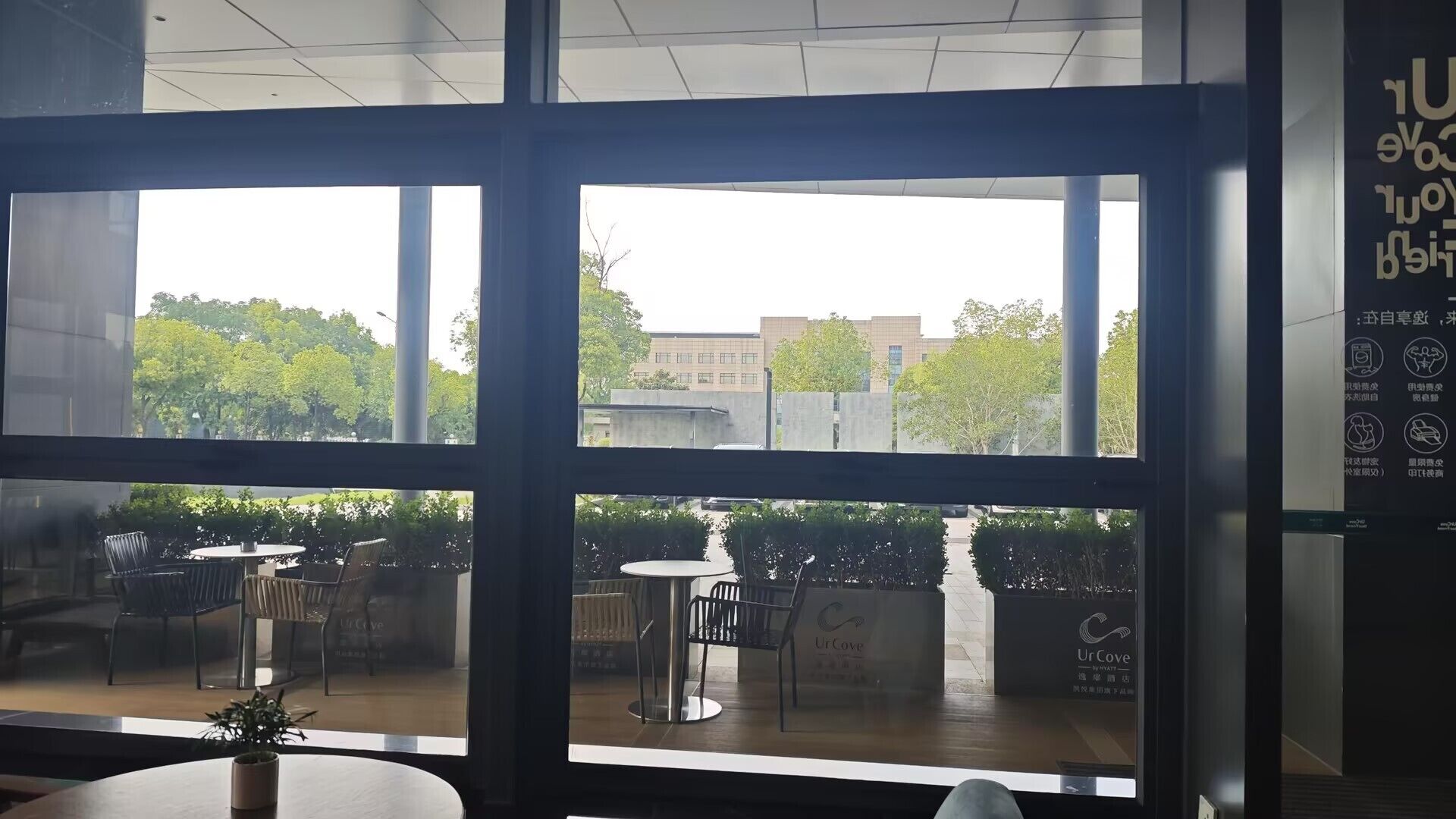 A view from inside a building with large windows, a balcony with outdoor seating, and a sign for 'UrCove by Hyatt'.