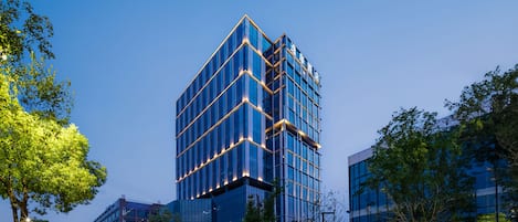 A modern high-rise building with a glass facade, surrounded by greenery and a well-maintained urban environment.