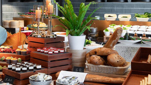 Diverse etenswaren gepresenteerd op houten kisten en tafels, waaronder gebak, brood en een potplant.