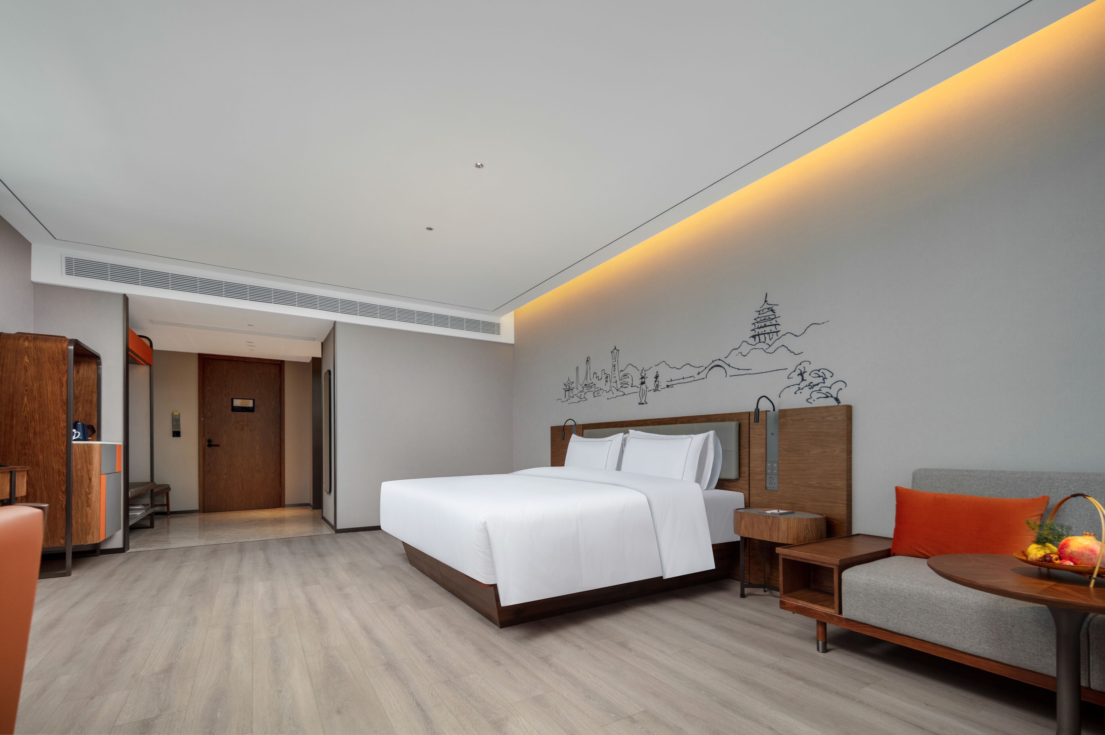 Een moderne hotelkamer met een bed, een bank, een tafeltje met fruit en een muurschildering.