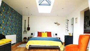 Une chambre avec une lucarne, un lit avec une literie aux couleurs vives, une chaise et un mur orné d’un motif de fruits.