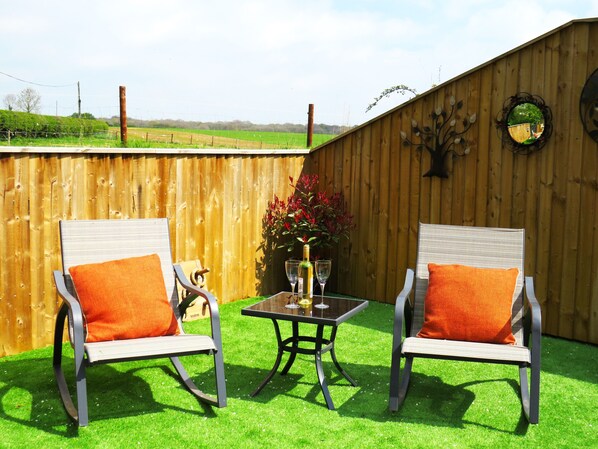 An outdoor seating area with two chairs and a table, a wooden fence, and a decorative tree wall. - Private Garden Room - Rural Village (Stamford)