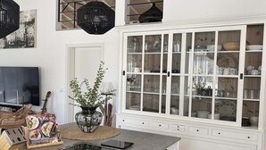 Una cocina con un armario grande blanco, una mesa de vidrio y un televisor.