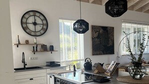 Una cocina moderna con armarios blancos, una isla central, un reloj de pared grande y una lámpara colgante.