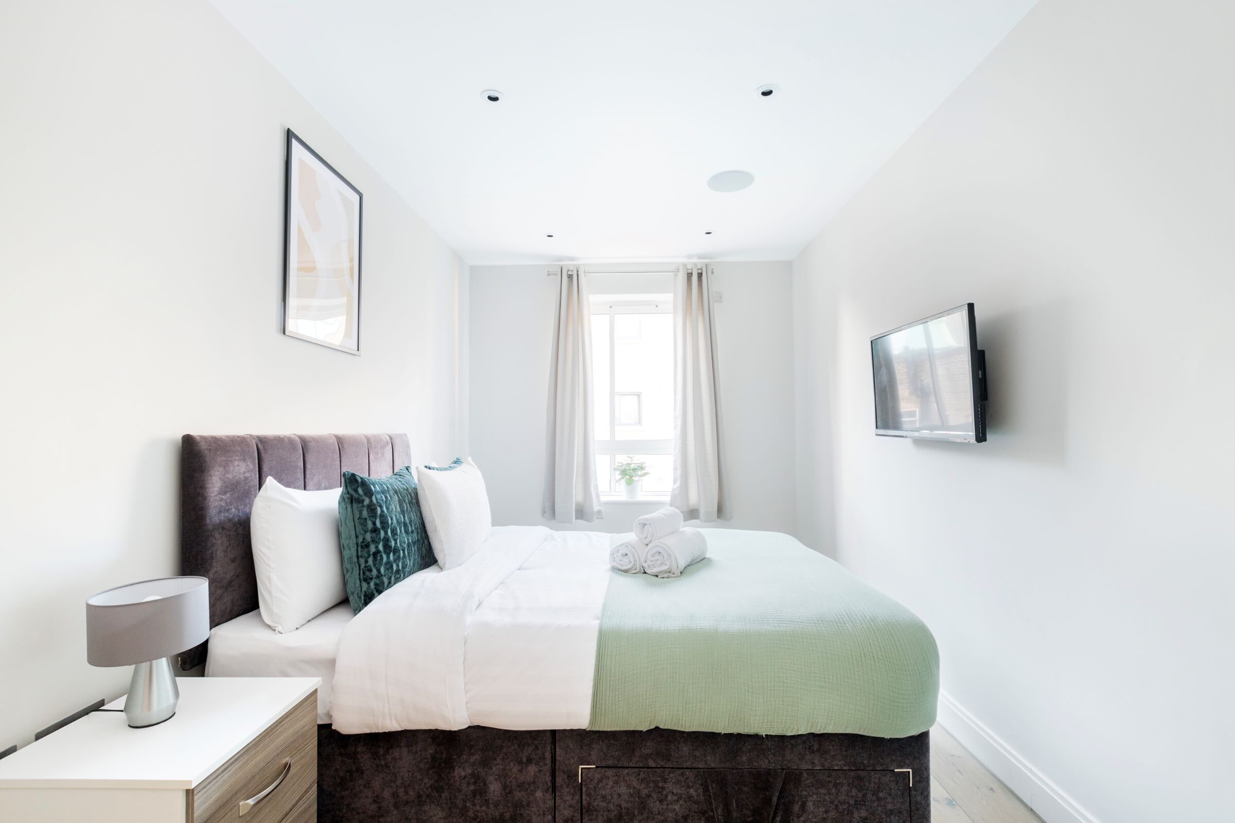 Une chambre à coucher moderne avec un lit, une table de chevet, une lampe et un téléviseur fixé au mur.
