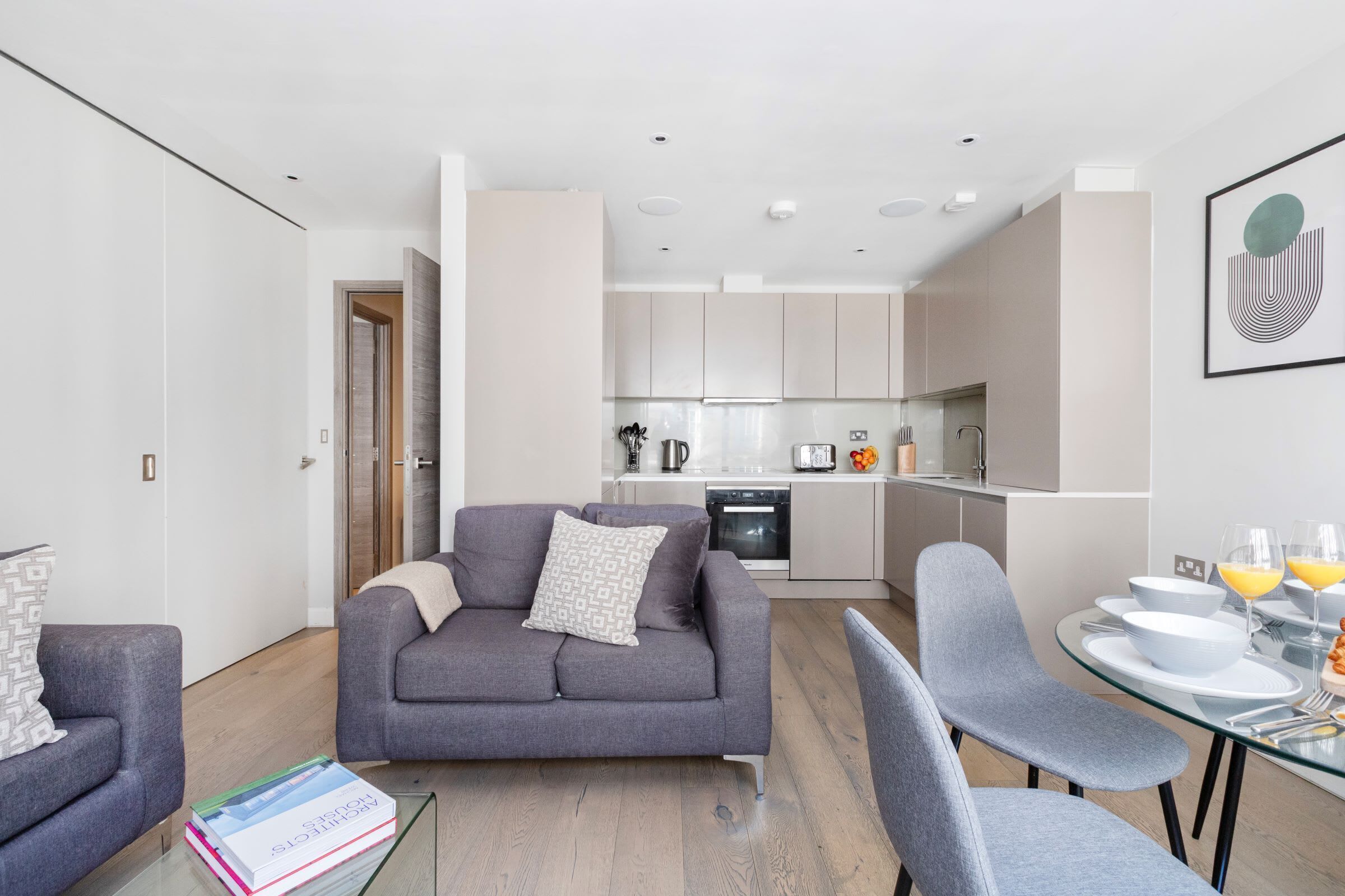 A modern living room with a grey sofa, a glass coffee table, and a dining area with a glass table and chairs.