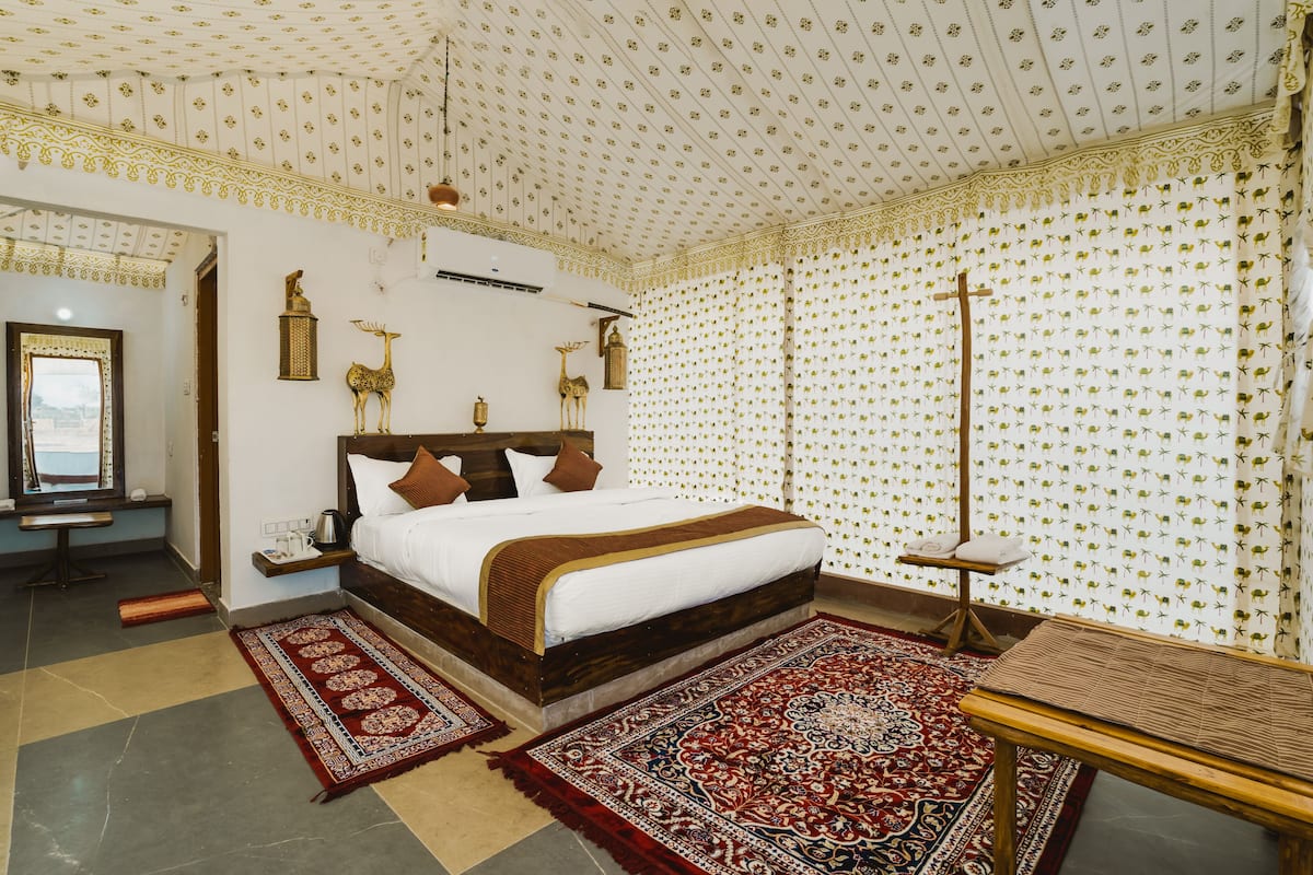 A bedroom with a large bed, a wooden nightstand, a table, and a patterned carpet.
