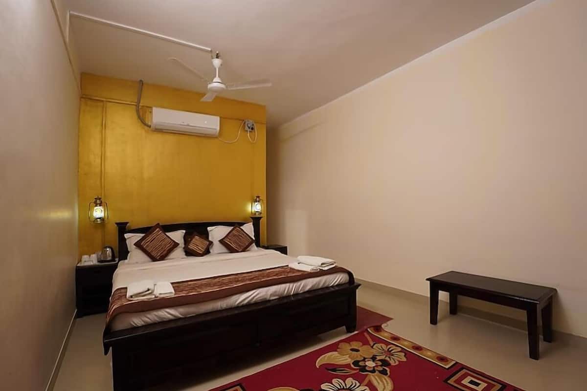 A bedroom with a bed, bedside lamps, a ceiling fan, an air conditioning unit, and a small table.