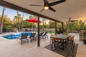 A covered outdoor area with a pool, lounge chairs, and a dining table.