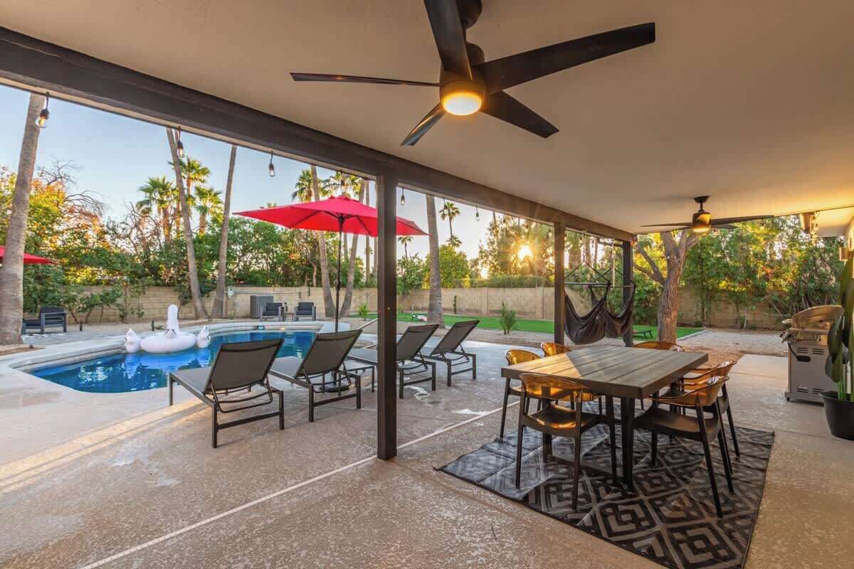 Une terrasse extérieure avec une piscine, des chaises longues, une table à manger et des ventilateurs de plafond.