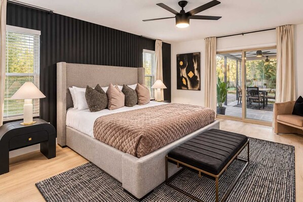 A modern bedroom with a large bed, a bench, a ceiling fan, and a view of the outdoors.