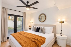 A hotel room with a bed, a ceiling fan, a round mirror, two bedside lamps, and a window with curtains.