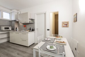 Une cuisine moderne avec des meubles blancs, un four à micro-ondes et un coin repas avec une table dressée pour deux personnes.