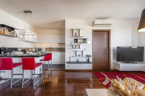 A modern kitchen with white cabinets, a red bar stool, a built-in island, and a flat-screen TV. - BnButler - Celio, 11 (Milano)