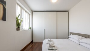 A hotel room with a bed, a window with curtains, a plant, and a wardrobe. - BnButler - Celio, 11 (Milano)