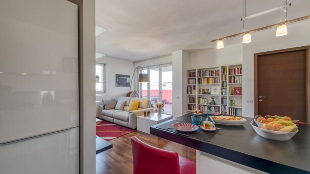 A modern kitchen with a dining area, a bookshelf, and a view of the living room. - BnButler - Celio, 11 (Milano)