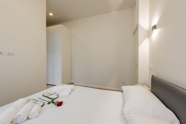A hotel room with a bed, towels, a rose, and a shower area.