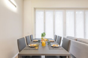Un coin repas avec une table dressée pour quatre personnes, une plante et un panier de fruits.