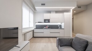 A modern kitchen with white cabinets, a microwave, and a sink. There is a grey sofa and a flat-screen TV in the living area. - BnButler - De Amicis, 25 (Milano)