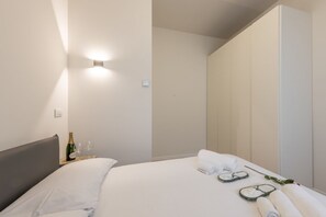 A modern hotel room with a bed, a nightstand with a bottle and glasses, a towel, and a mirror. - BnButler - De Amicis, 25 (Milano)