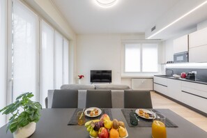 A modern kitchen with a dining table set for breakfast, a sofa, and a TV in the background. - BnButler - De Amicis, 25 (Milano)